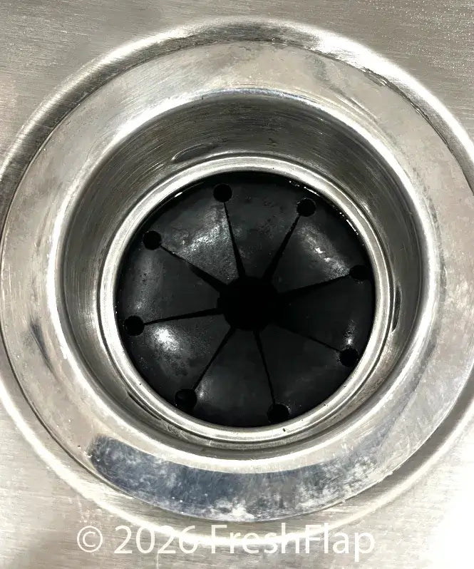 Close-up of a kitchen sink drain with a clean and shiny black rubber splash guard.