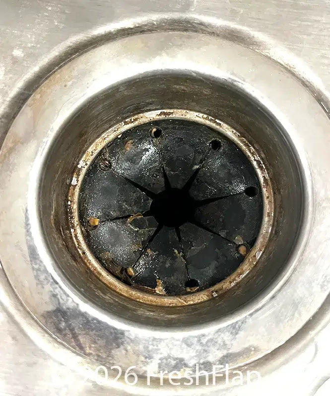 Close-up of a kitchen sink garbage disposal drain with a dirty black rubber splash guard with visible chunks of debris and gunk.