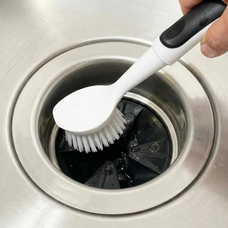 Person using a white and black scrub brush on the garbage disposal rubber flaps in a kitchen sink